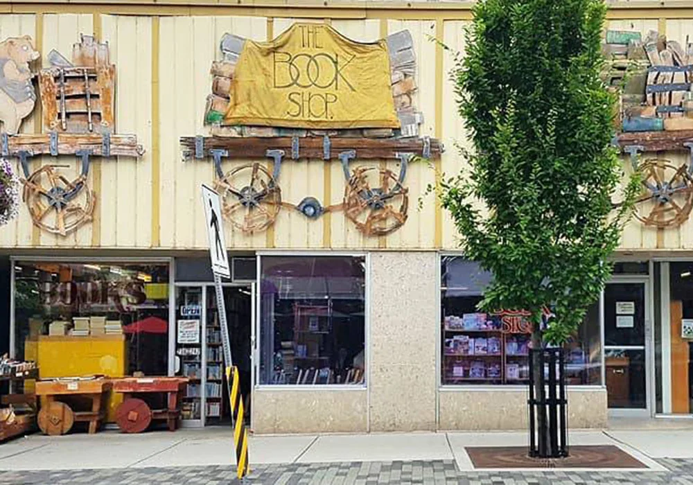 A charming storefront with a tree nearby and a sign, surrounded by eclectic shops and vibrant downtown life.