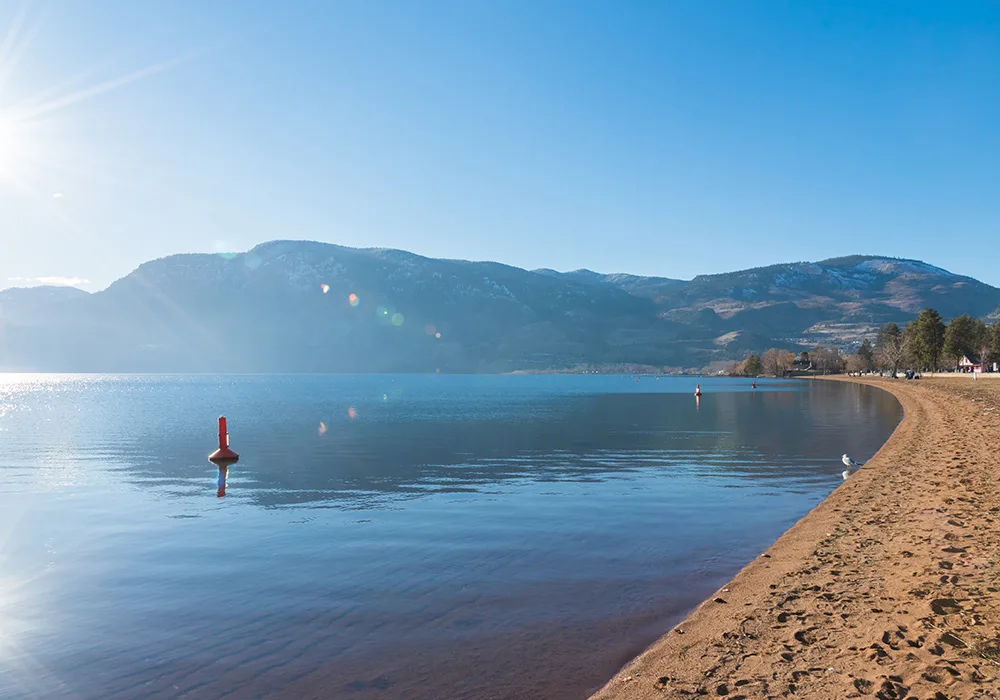 A picturesque beach with a calm lake and stunning mountains looming in the distance, creating a perfect natural escape.