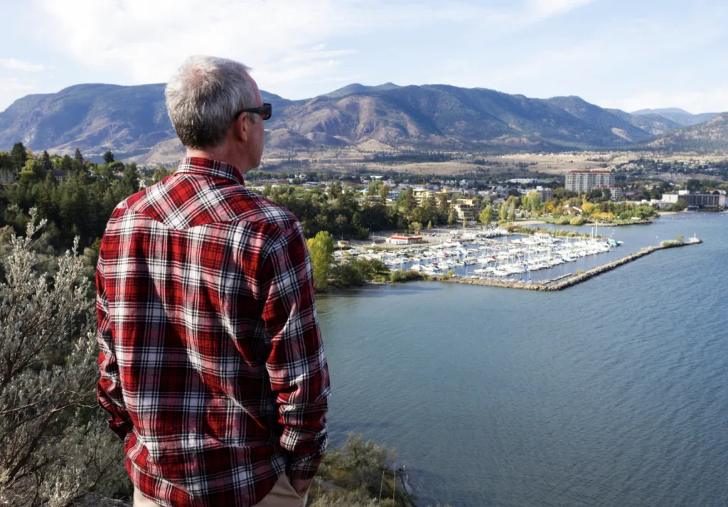 A man in a plaid shirt gazes thoughtfully at the calm lake, enjoying the serene view.